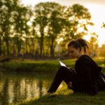 Studying Abroad - woman sitting on grass field beside body of water during golden hour