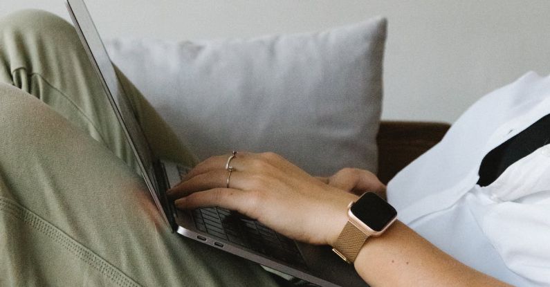 Smart Watches Benefits - Side view of crop unrecognizable female freelancer in casual clothes and smartwatch lying on comfortable sofa and working remotely on laptop