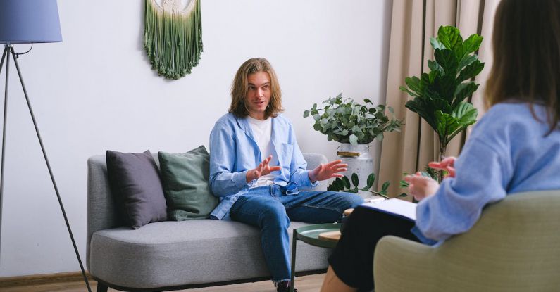Difficult Clients - Worried male patient sitting on couch while having conversation about problems with unrecognizable professional psychologist during psychotherapy appointment in office